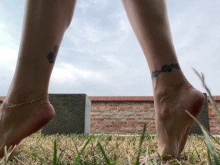 Slow motion milf barefoot in grass, wrinkled soles and red toes